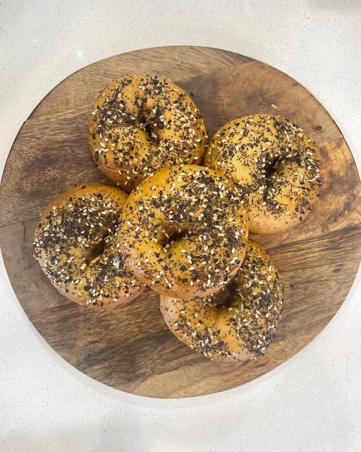 Five seeded everything bagels stacked on a round wooden board.