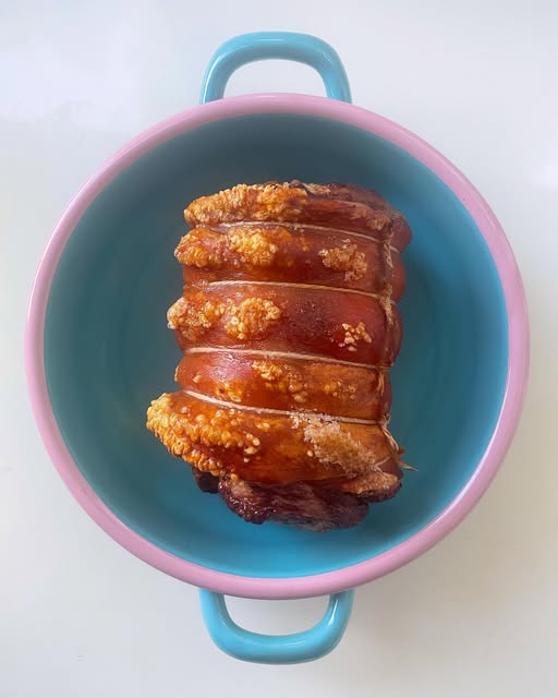 A rolled roast pork with crisp crackling resting in a pink and blue dish.