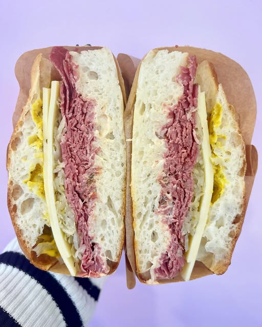 A house-made focaccia sandwich cut in half, layered with corned beef, cheese, pickles and slaw.