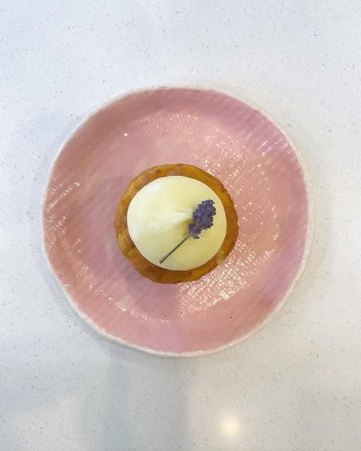 A small lemon tart topped with a sprig of lavender on a pink handmade plate.